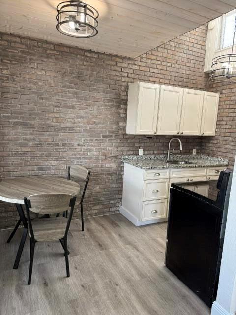 A kitchen and dining area features a brick wall, light wood flooring, and white cabinetry — 131 S Federal Highway # 3, FL 33460, FL