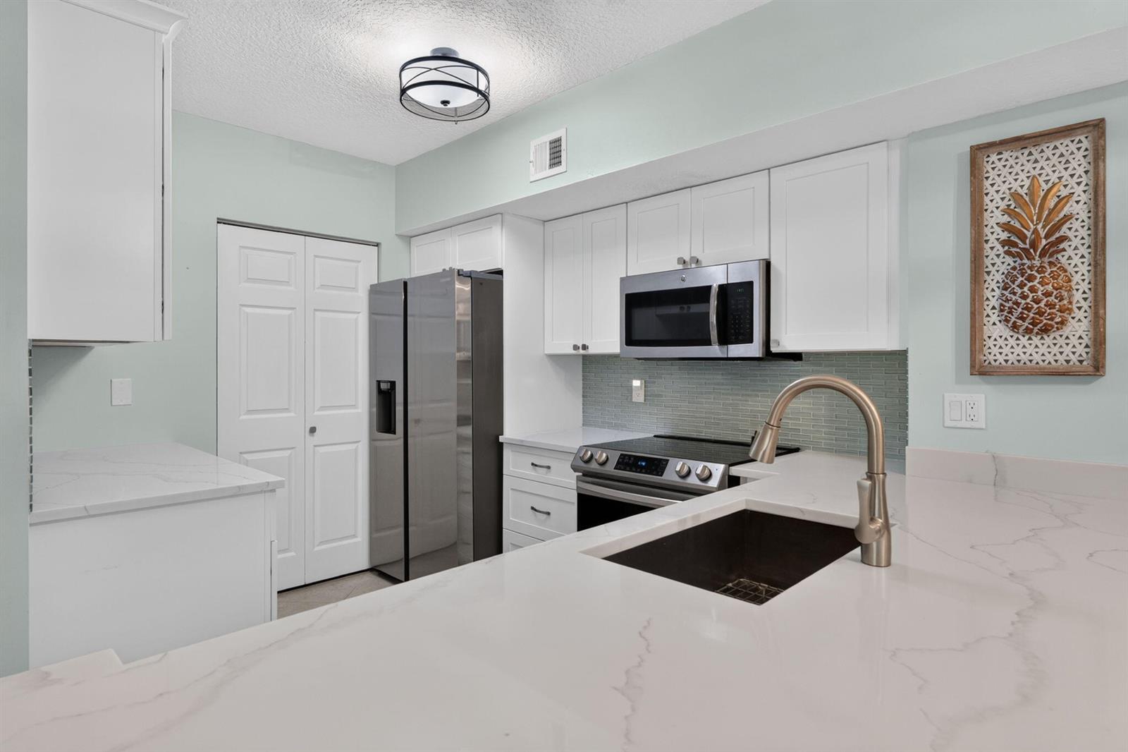 A kitchen features white cabinets, stainless steel appliances, a quartz countertop, and a tile backsplash — 236 Village Boulevard, Tequesta FL 33469, TEQUESTA, FL
