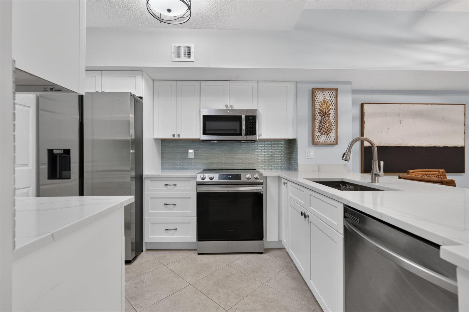 A modern kitchen features white cabinetry, stainless steel appliances, and a light-colored tile floor — 236 Village Boulevard, Tequesta FL 33469, TEQUESTA, FL