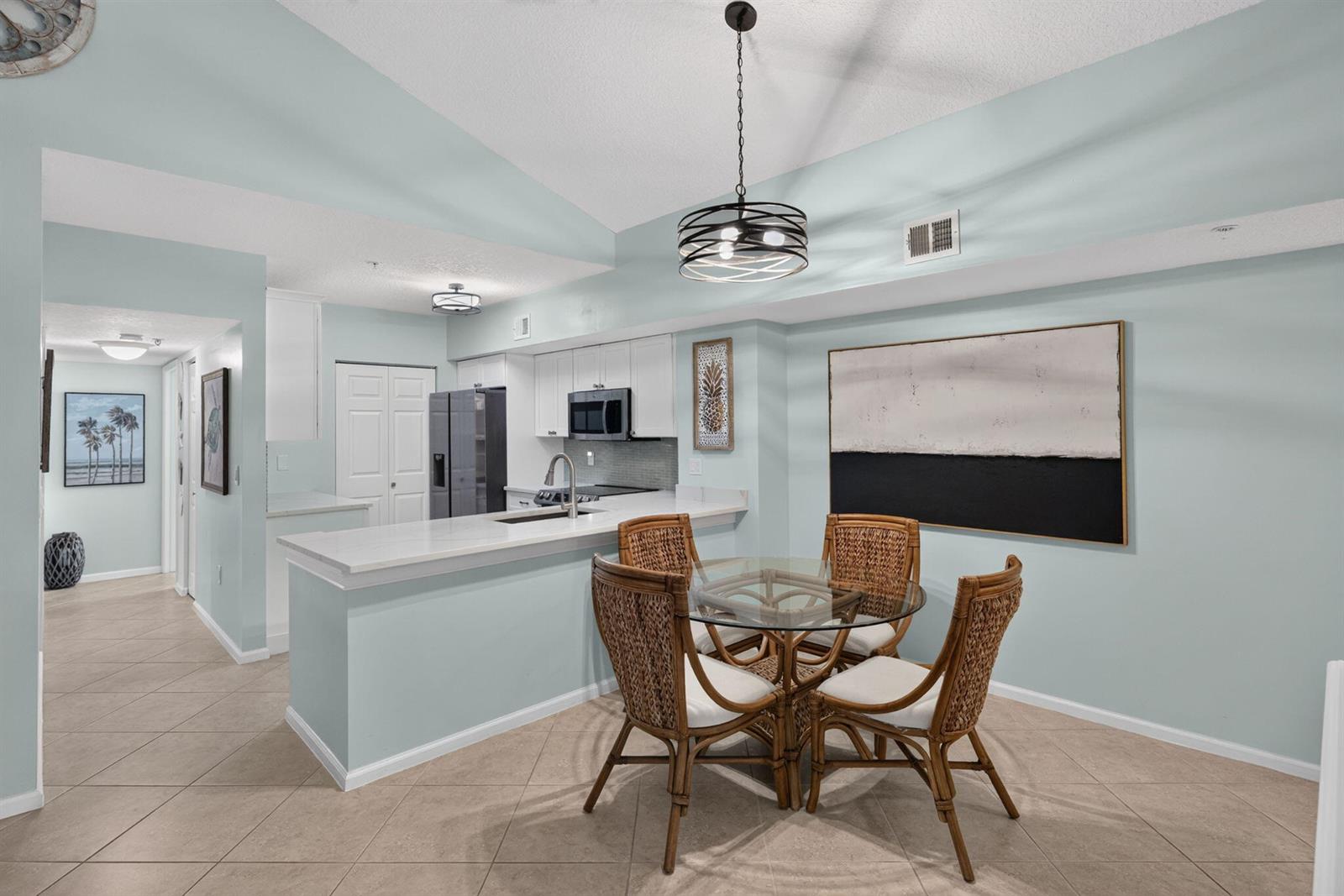 A kitchen with white cabinets and a dining area featuring a glass-topped wicker table — 236 Village Boulevard, Tequesta FL 33469, TEQUESTA, FL