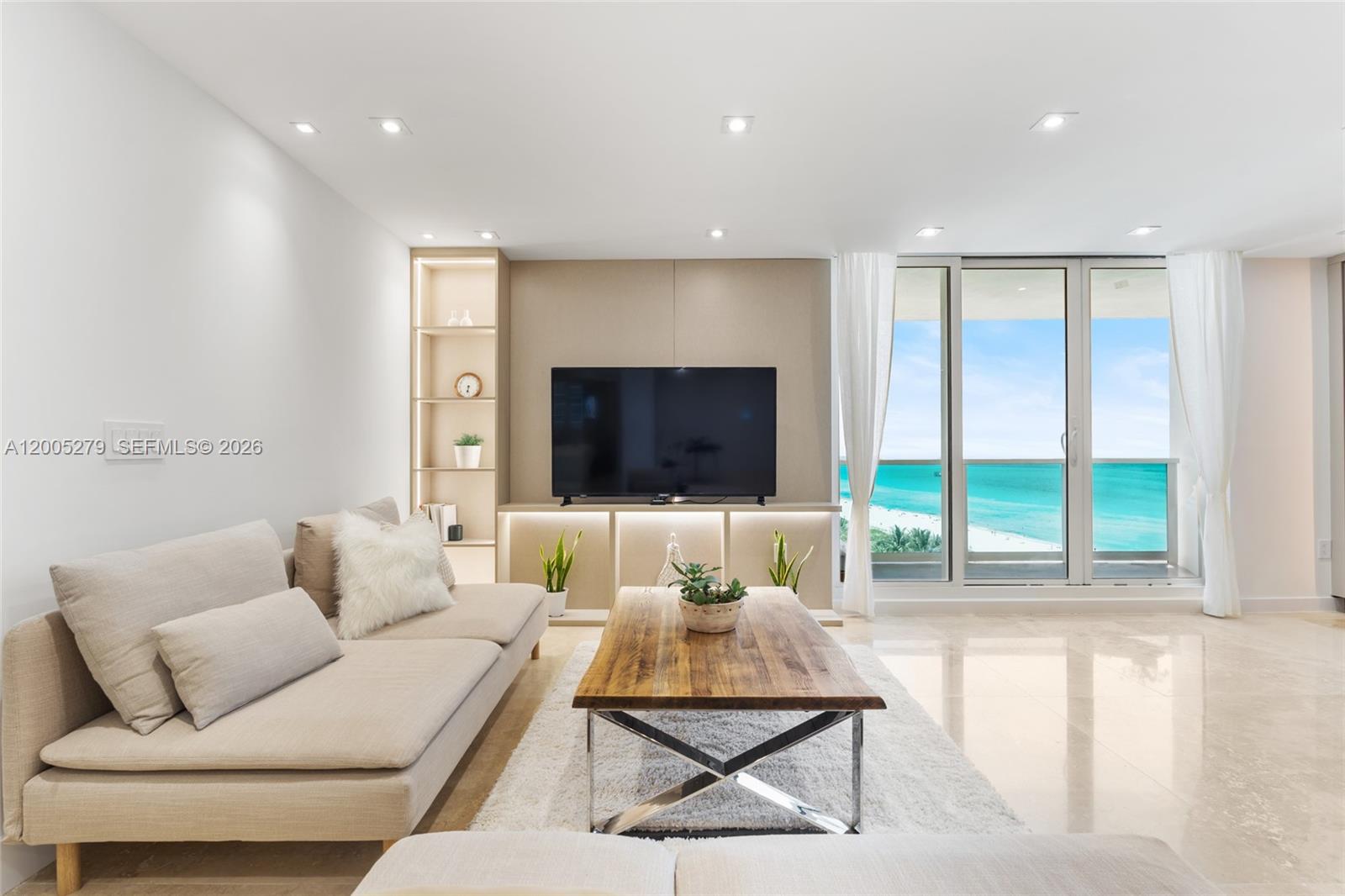 A living room features a neutral sofa, wooden coffee table, and a view of the ocean — 2301 Collins # 1011, Miami Beach FL 33139, MIAMI BEACH, FL