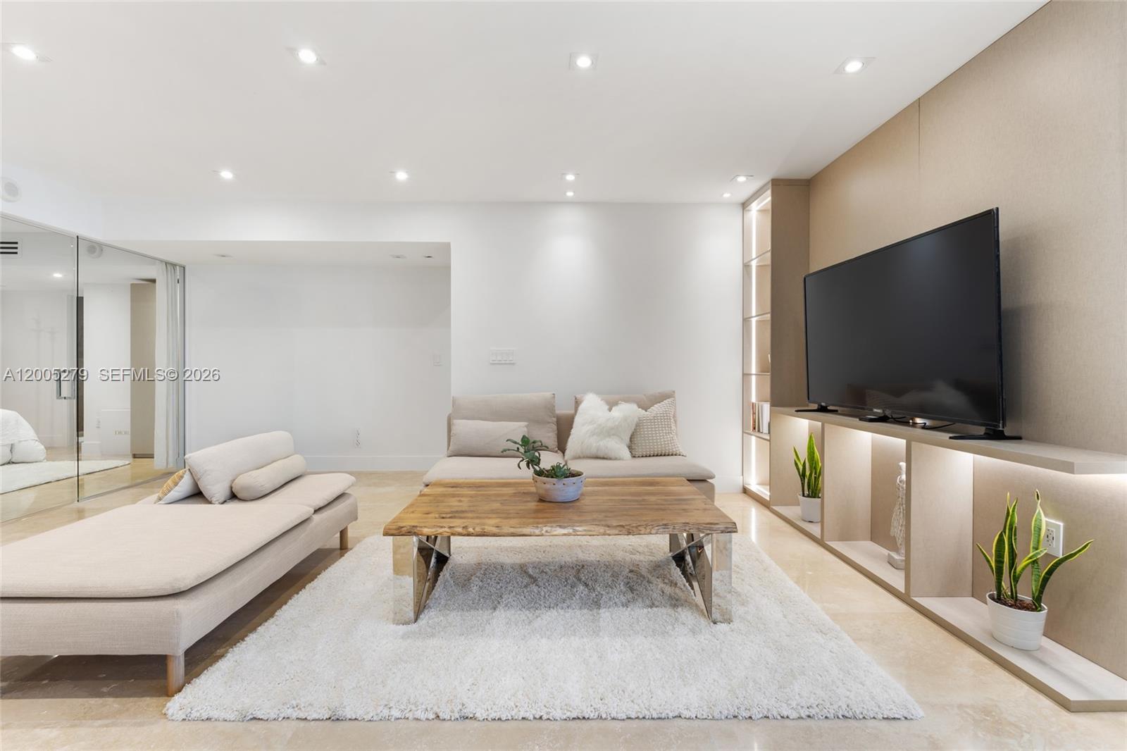A modern living room features a beige sofa, a wooden coffee table, and built-in shelving — 2301 Collins # 1011, Miami Beach FL 33139, MIAMI BEACH, FL