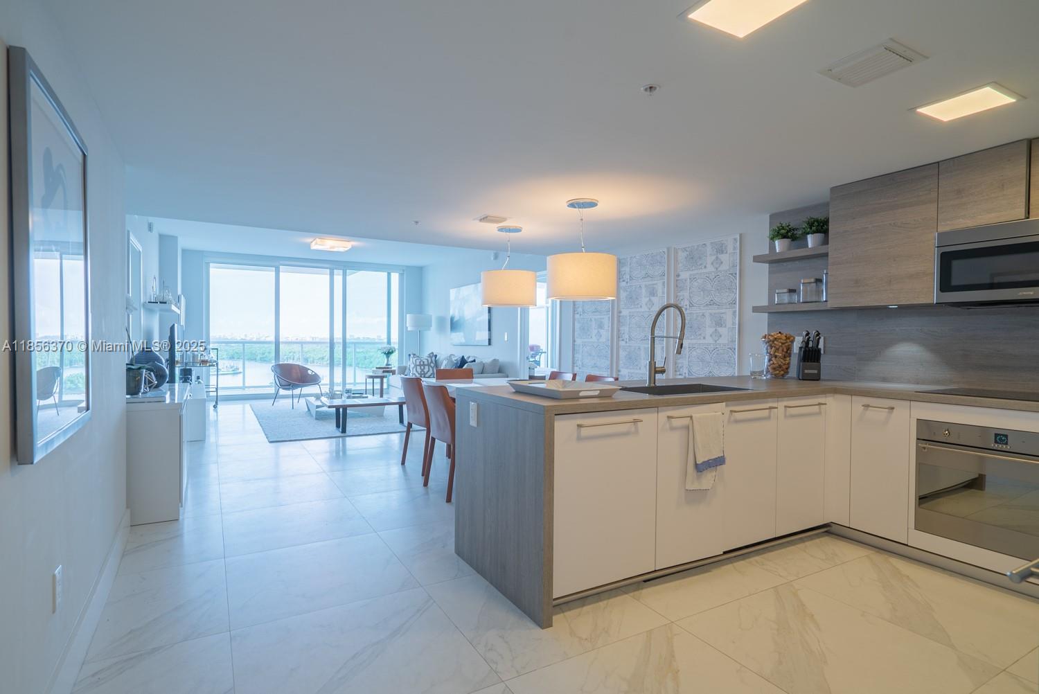 A modern kitchen with white cabinets and wood accents opens into a bright living area — SUNNY ISLES BEACH, FL