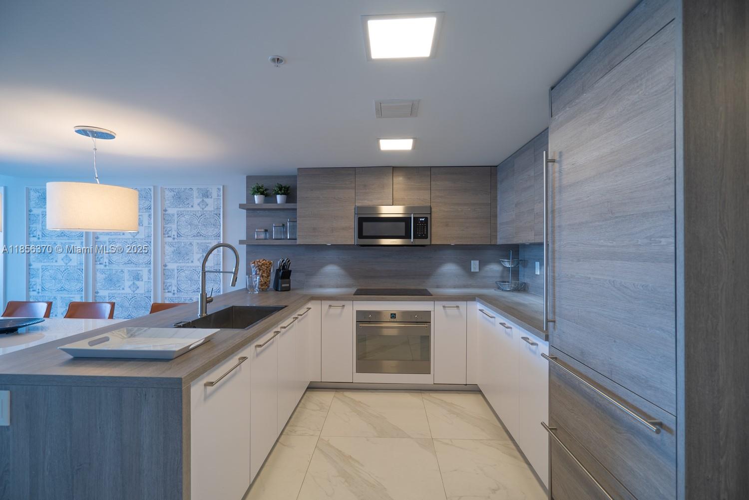 A modern kitchen features two-toned cabinetry, stainless steel appliances, and a marble-patterned tile floor — SUNNY ISLES BEACH, FL