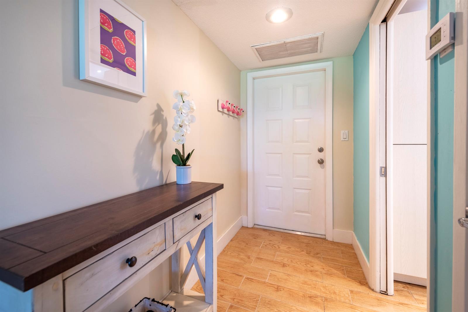 A hallway features a wooden console table, a white door, and light-colored tile flooring — 2651 S Course Drive # 308, Pompano Beach FL 33069, POMPANO BEACH, FL