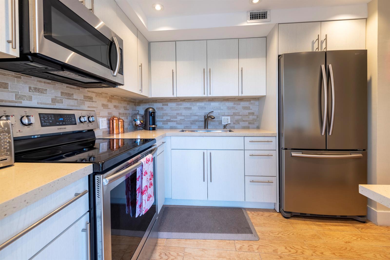A kitchen features white cabinets, stainless steel appliances, a tiled backsplash, and light wood flooring — 2651 S Course Drive # 308, Pompano Beach FL 33069, POMPANO BEACH, FL