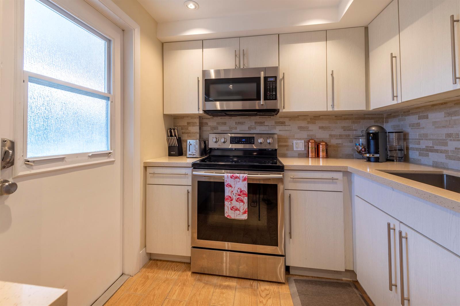 A kitchen features light wood cabinets, stainless steel appliances, and a tan tile backsplash — 2651 S Course Drive # 308, Pompano Beach FL 33069, POMPANO BEACH, FL