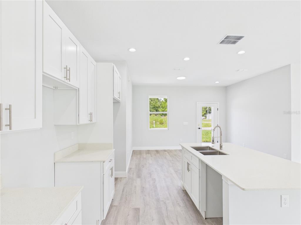 A bright kitchen features white cabinets, quartz countertops, a center island, and light wood flooring — 12807 SW 73RD AVENUE ROAD, OCALA, FL