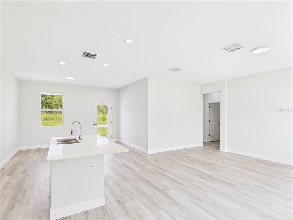 A bright, open-concept kitchen and living area features light wood-look flooring and a white island — 12807 SW 73RD AVENUE ROAD, OCALA, FL