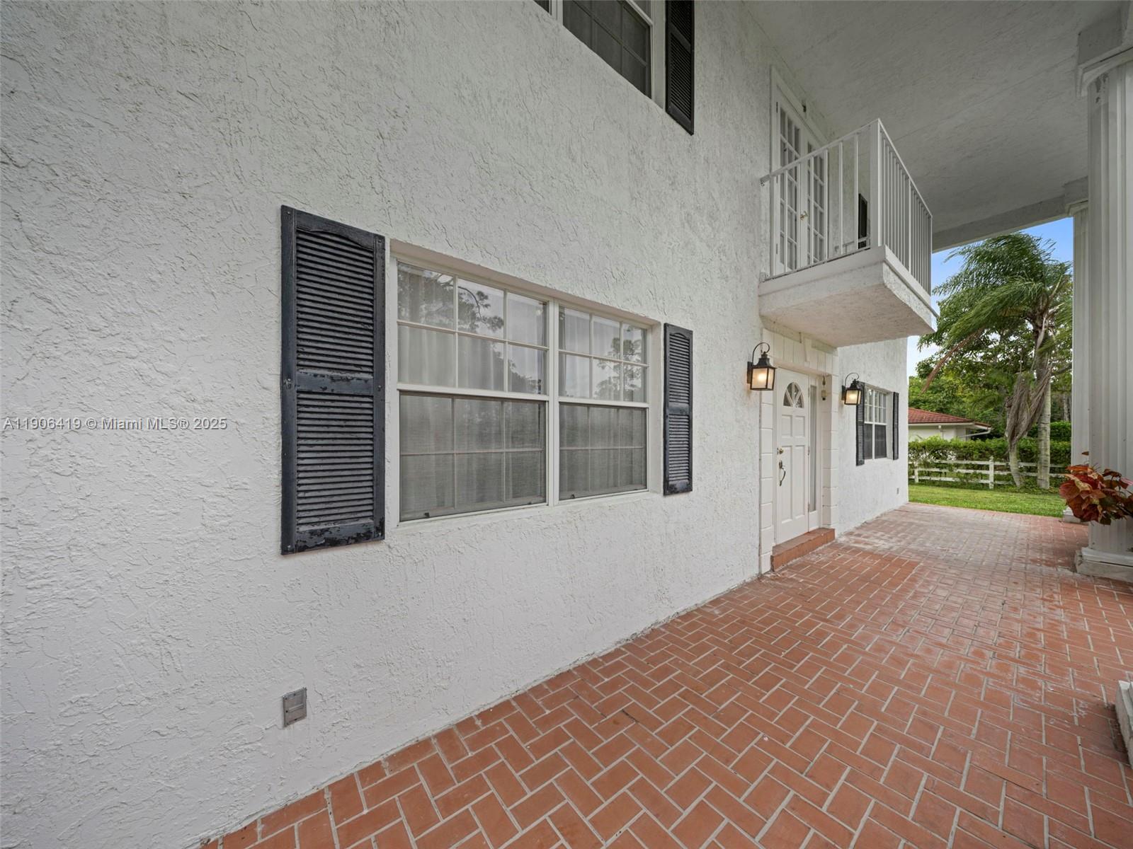 A white stucco house exterior features a brick patio, a balcony, and black shutters — 6365 NW 79th Way, Parkland FL 33067, PARKLAND, FL