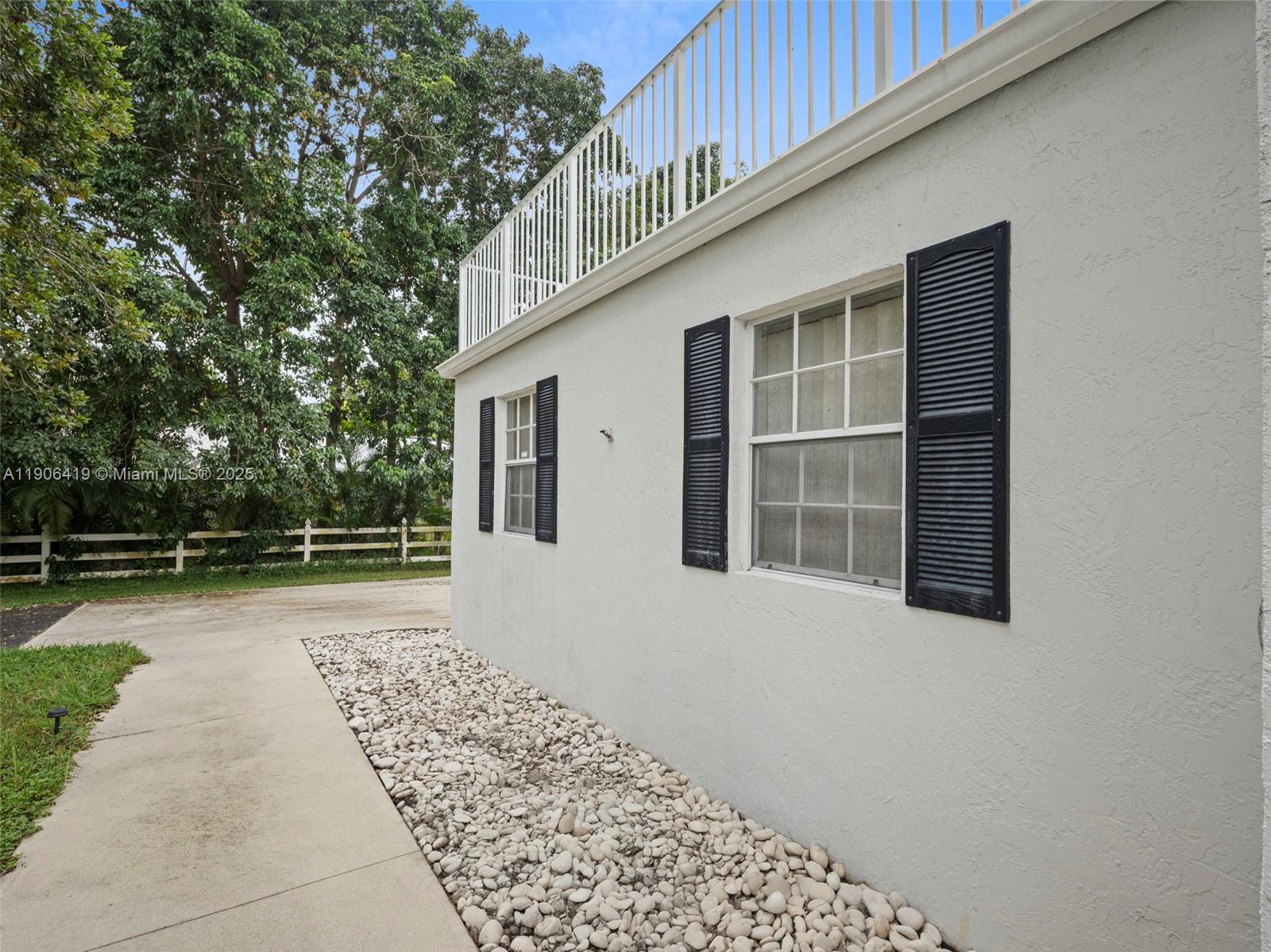 The exterior of a white house features black shutters, a balcony railing, and a rock garden — 6365 NW 79th Way, Parkland FL 33067, PARKLAND, FL