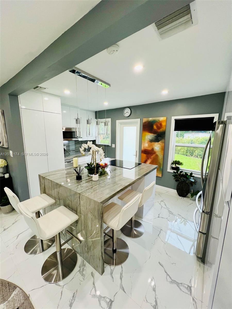 A modern kitchen features a marble-topped island with white bar stools and marble flooring — 920 NE 108th St # 0, Biscayne Park FL 33161, BISCAYNE PARK, FL