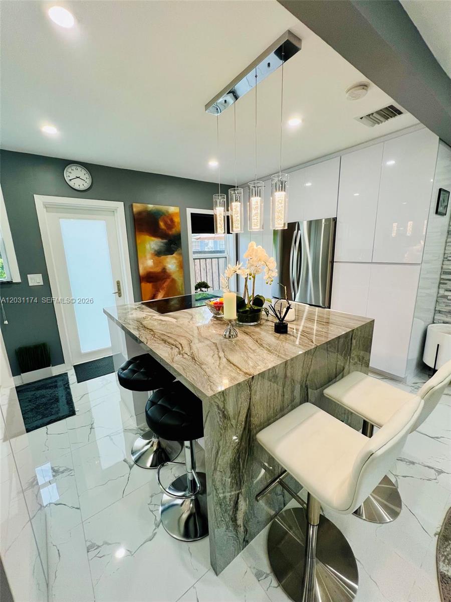 A modern kitchen features a stone waterfall island, white cabinetry, and white marble-patterned tile floors — 920 NE 108th St # 0, Biscayne Park FL 33161, BISCAYNE PARK, FL