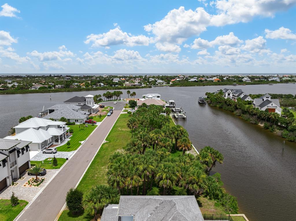 An aerial view shows a coastal neighborhood with houses, palm trees, and a waterway — 142 SEASIDE POINT, FLAGLER BEACH, FL