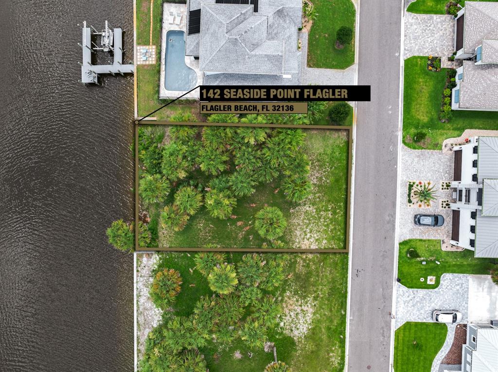 This aerial view shows a vacant, tree-covered waterfront lot situated between two developed residential properties — 142 SEASIDE POINT, FLAGLER BEACH, FL