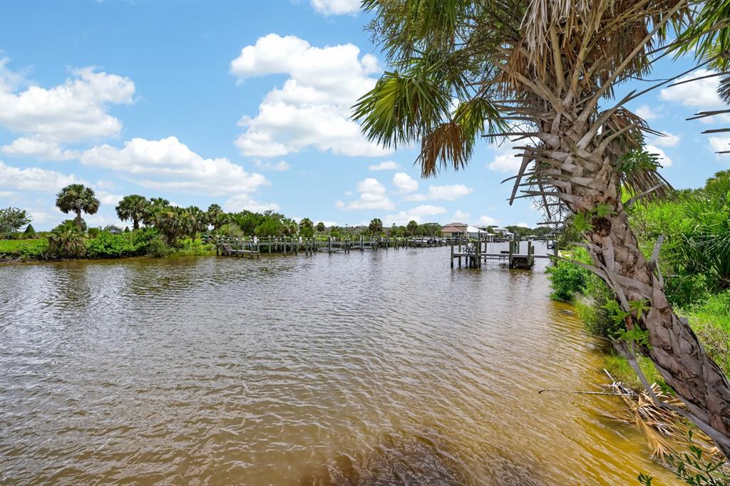 A canal view with wooden boat docks, palm trees, and a blue sky with clouds — 142 SEASIDE POINT, FLAGLER BEACH, FL