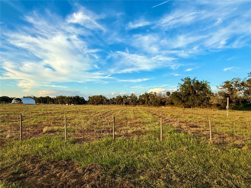 A fenced, grassy field under a blue sky with a distant metal structure — 2902 SE PIGGYBACK ROAD, ARCADIA, FL