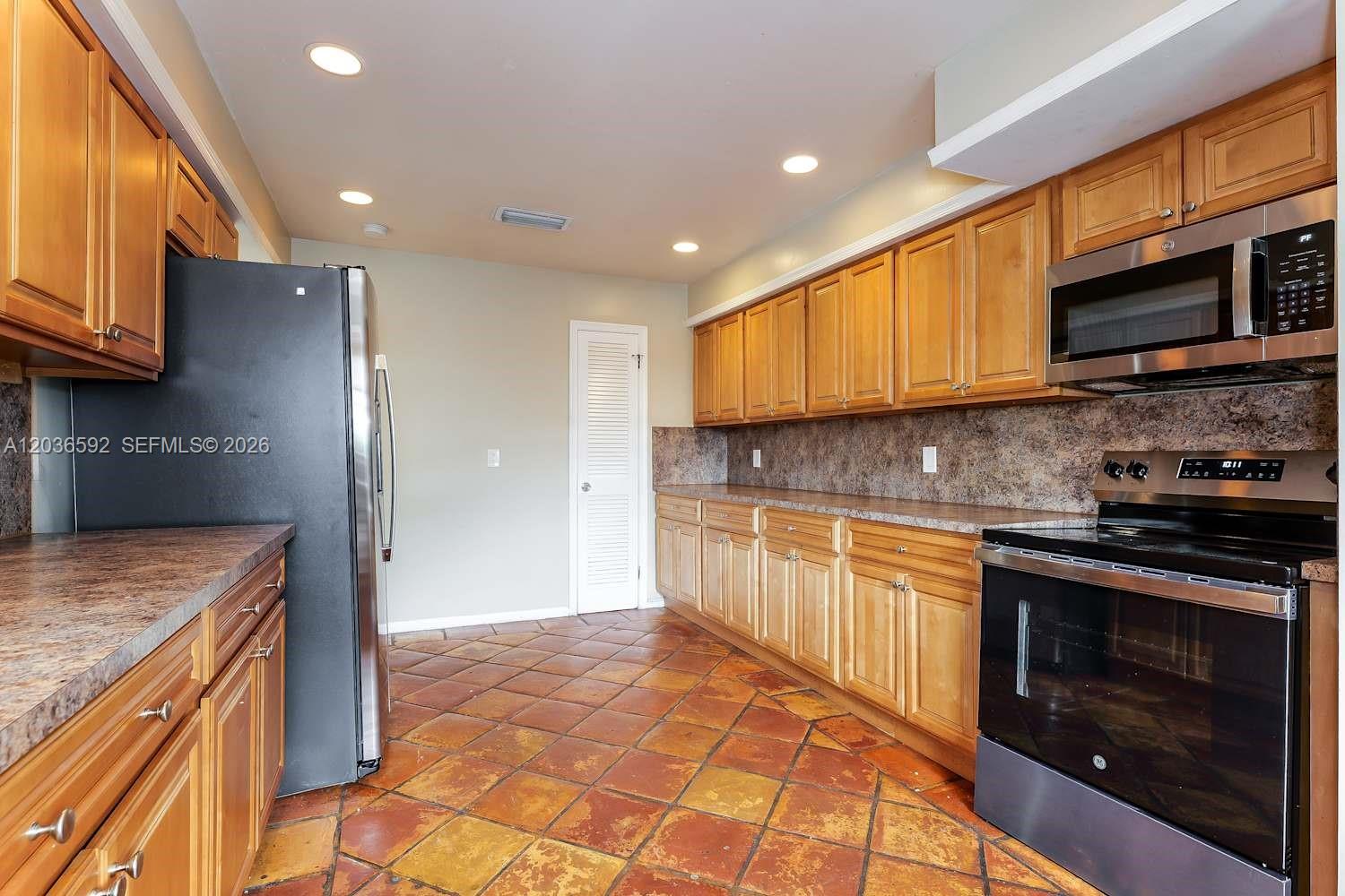 A kitchen features wooden cabinets, stainless steel appliances, and brown tile flooring — BOYNTON BEACH, FL