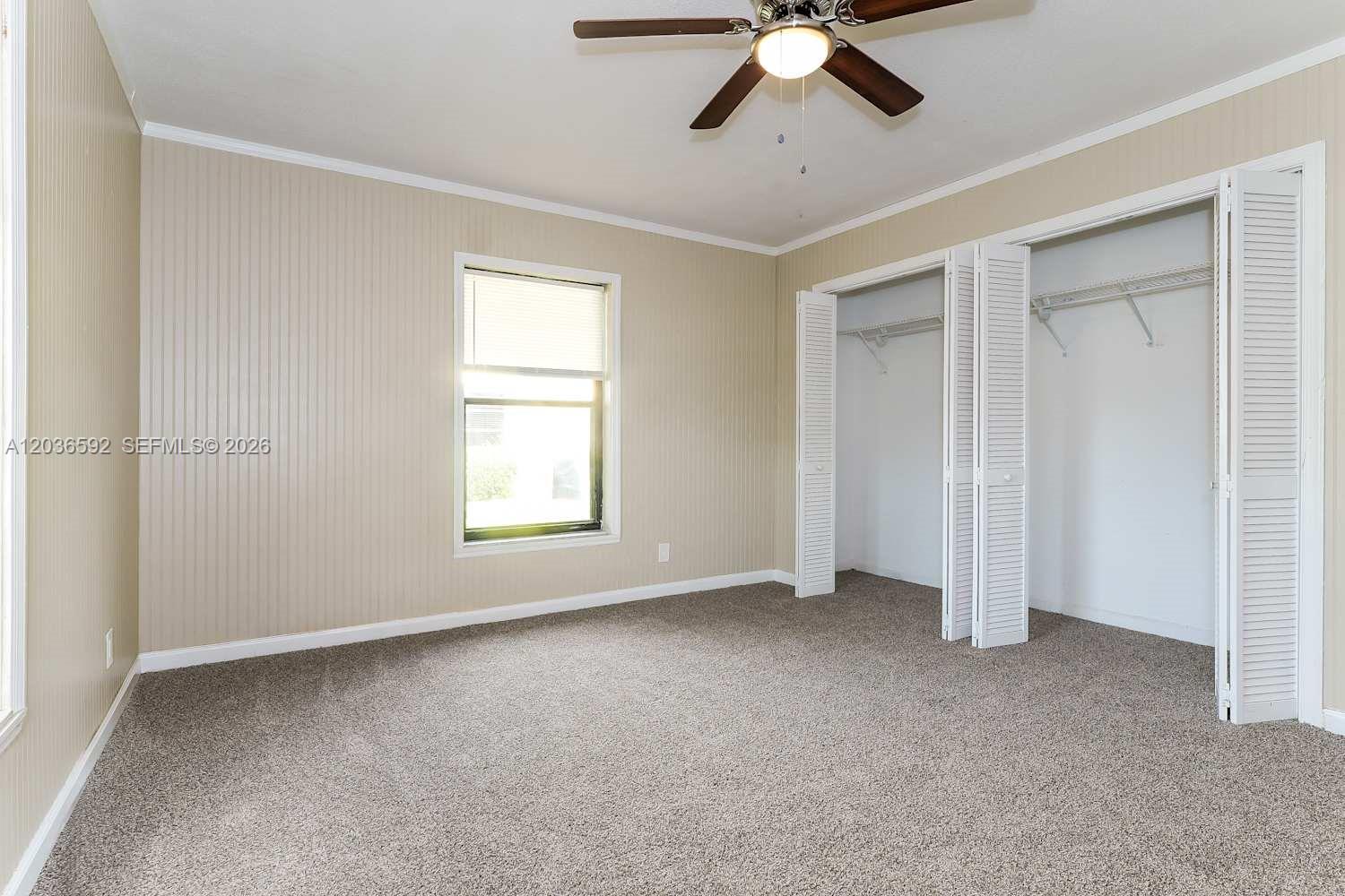 A bedroom features beige vertical-paneled walls, gray carpeting, a ceiling fan, and a double-door closet — BOYNTON BEACH, FL