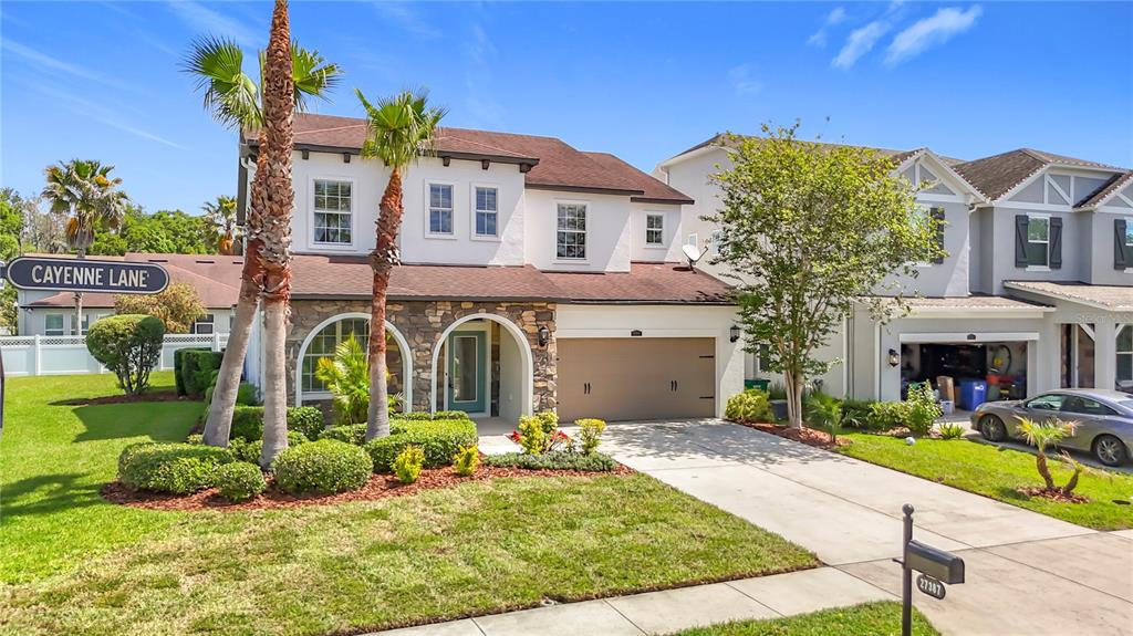 A two-story suburban house with a stone facade, a two-car garage, and palm trees — 27387 CAYENNE LANE, WESLEY CHAPEL, FL