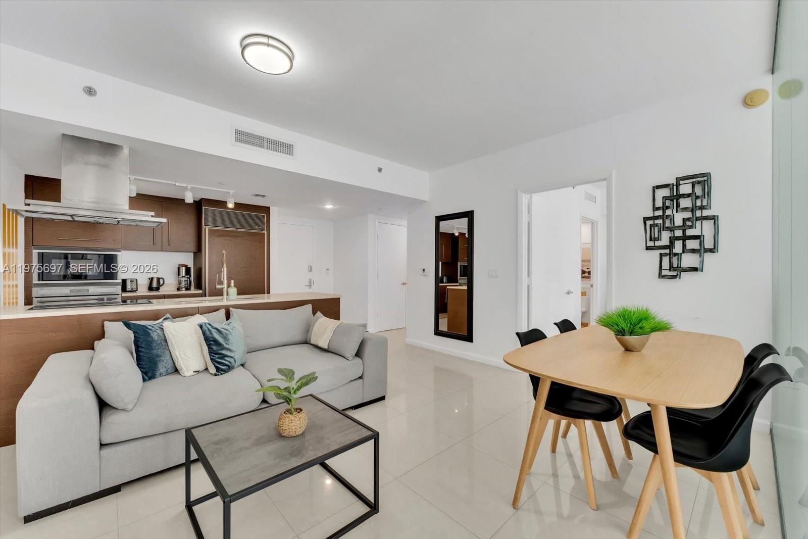 A modern open-concept living area features a kitchen, gray sofa, and a wooden dining table — 485 Brickell Ave # 1807, Miami FL 33131, MIAMI, FL