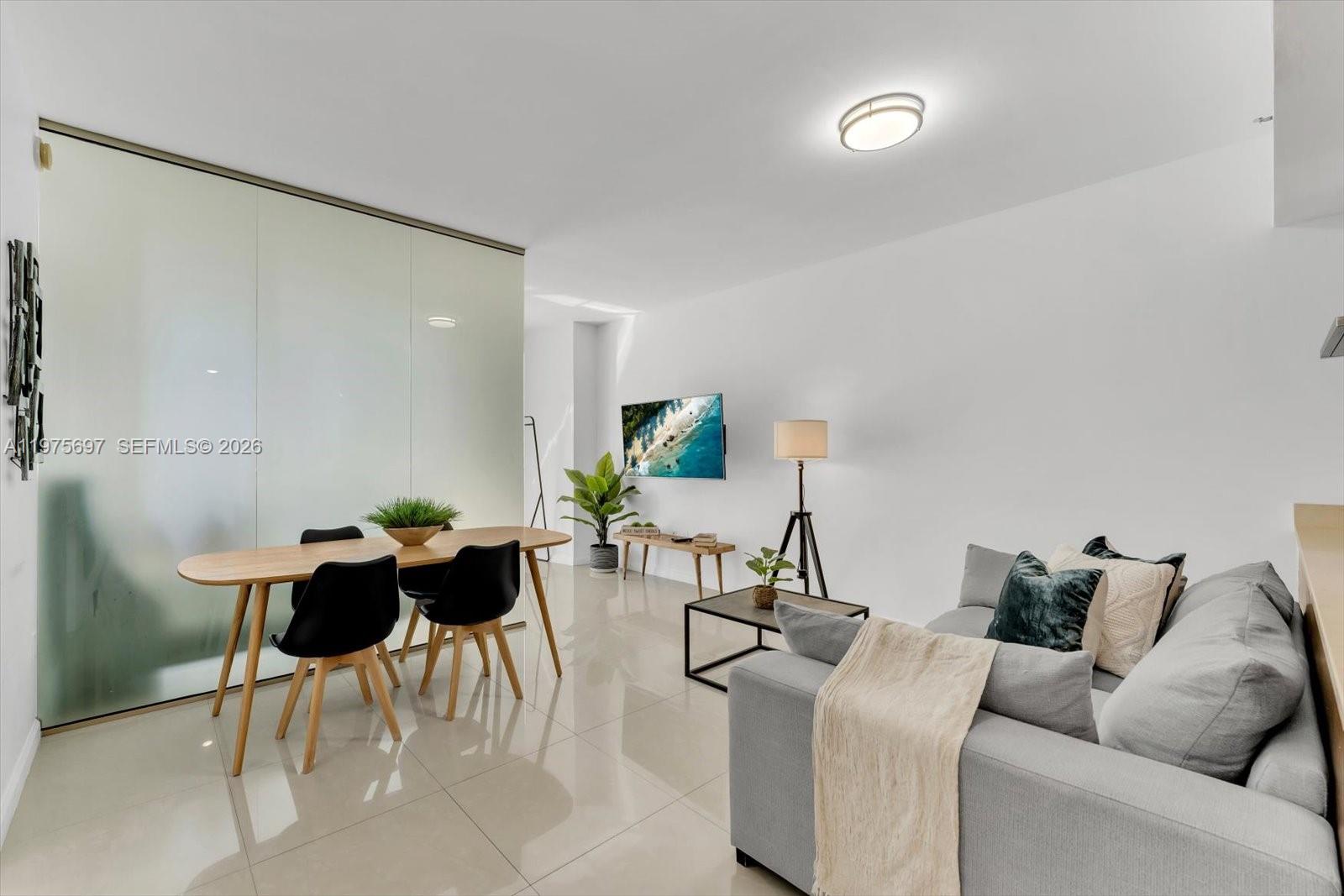 A modern living and dining area features white walls, tile flooring, and a glass partition — 485 Brickell Ave # 1807, Miami FL 33131, MIAMI, FL