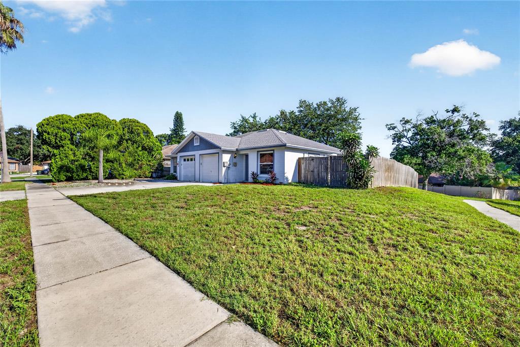 A single-story house with a two-car garage and a large front lawn under a blue sky — 2699 MACKLIN COURT, PALM HARBOR, FL