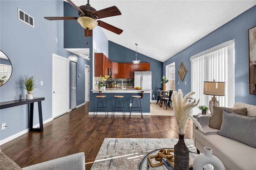 An open-concept living room and kitchen with blue walls, wood floors, and a vaulted ceiling — 2699 MACKLIN COURT, PALM HARBOR, FL