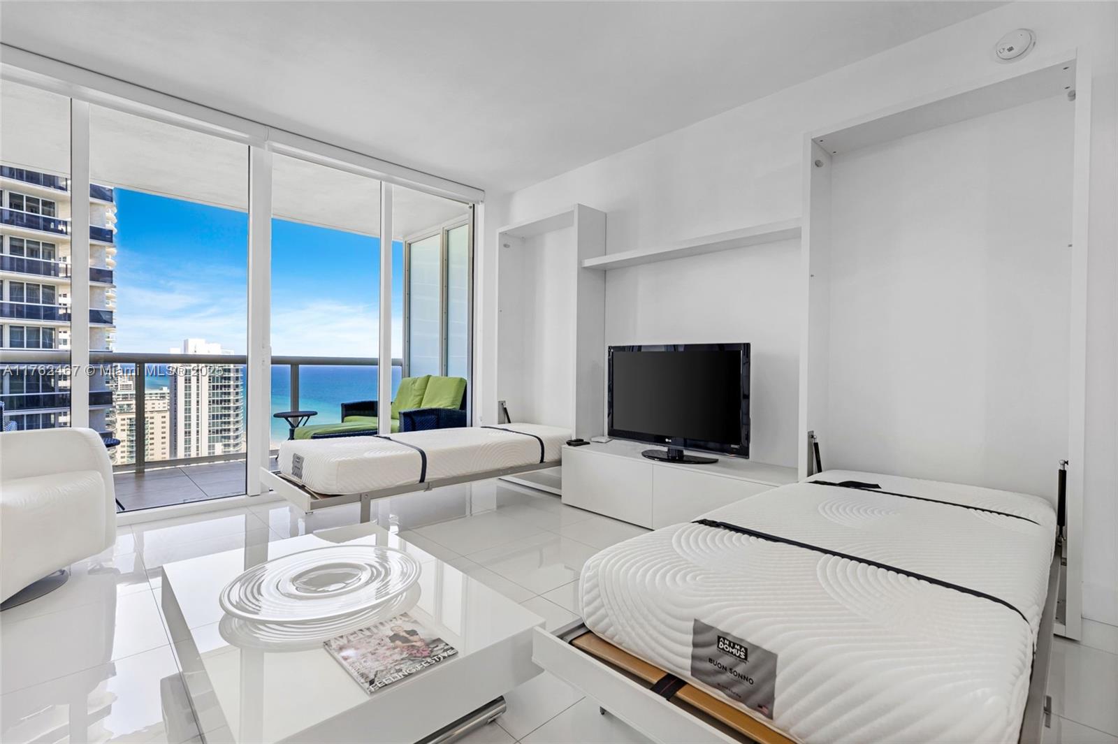 A bright living room features two white Murphy beds, a television, and a balcony with ocean views — 1830 S Ocean Dr # 2609, Hallandale Beach FL 33009, HALLANDALE BEACH, FL