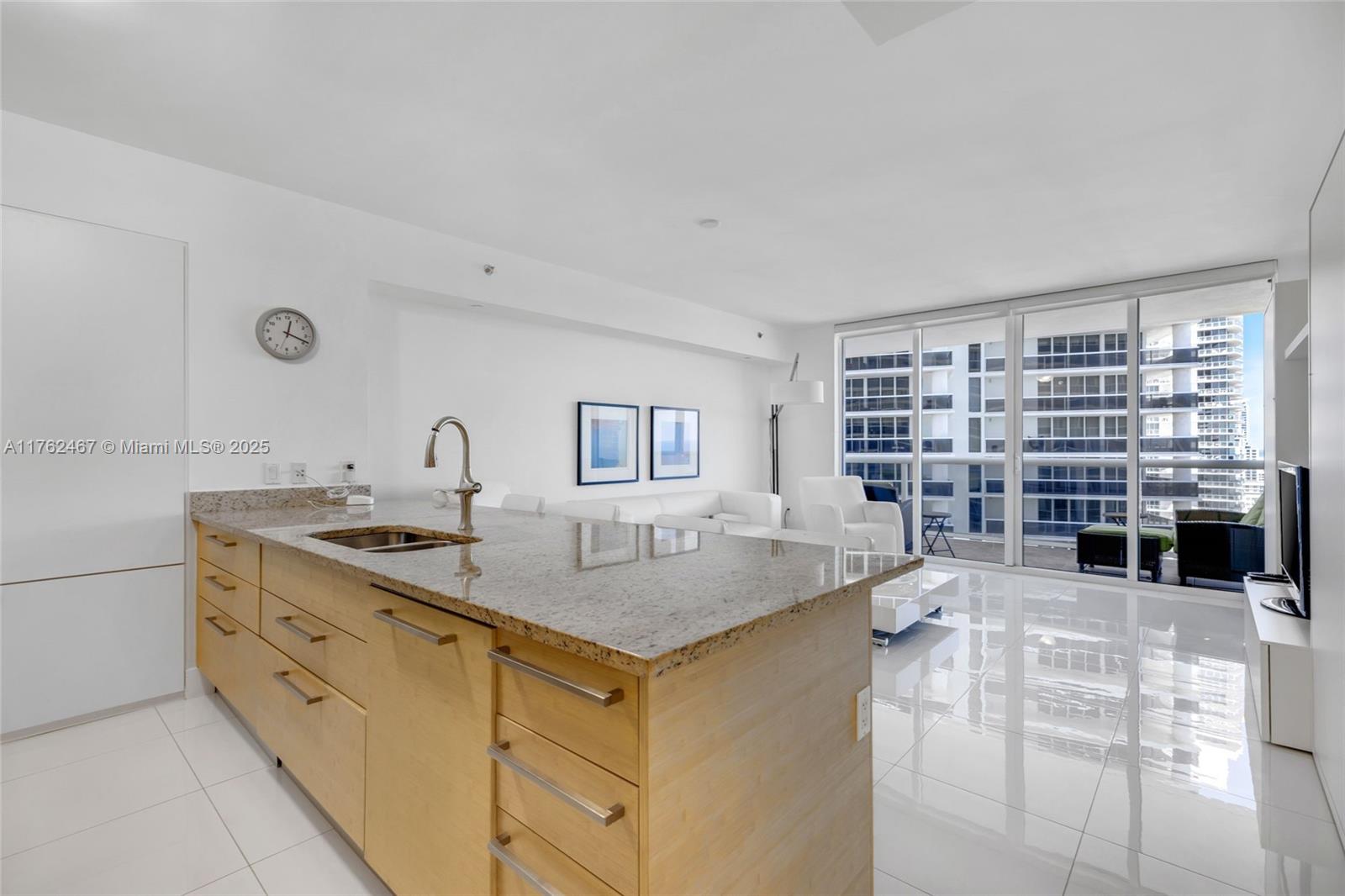 A modern kitchen with a granite island and light wood cabinets overlooks a bright living area — 1830 S Ocean Dr # 2609, Hallandale Beach FL 33009, HALLANDALE BEACH, FL