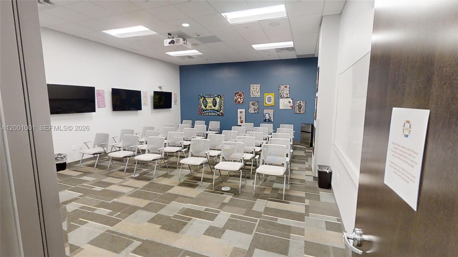 A conference room features rows of chairs, wall-mounted televisions, and artwork on a blue wall — 1501 Biscayne Blvd, FL 33132, FL