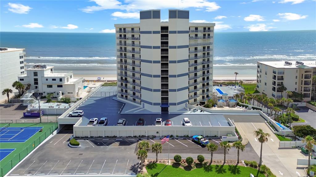 An aerial view shows a multi-story beachfront condominium building with a parking lot and pool — 5207 S ATLANTIC AVENUE UNIT 323, NEW SMYRNA BEACH, FL