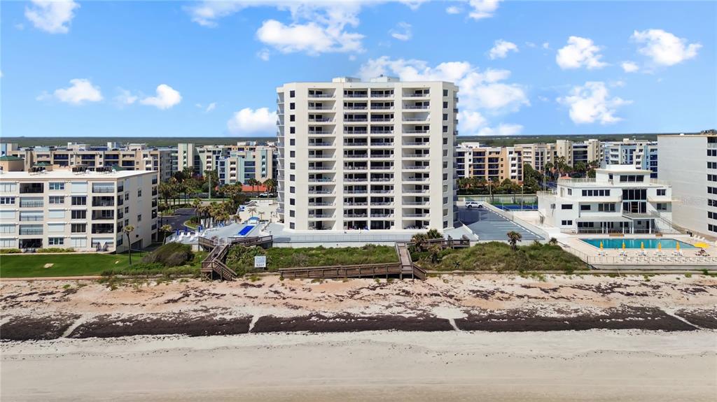 An aerial view shows a tall beachfront condominium building with a pool and wooden walkways — 5207 S ATLANTIC AVENUE UNIT 323, NEW SMYRNA BEACH, FL