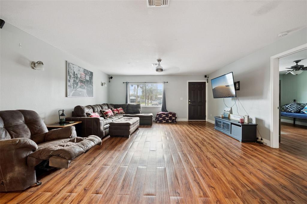 A living room features wood-look flooring, a sectional sofa, a recliner, and a wall-mounted television — 1050 CRYSTAL BOWL CIRCLE, CASSELBERRY, FL