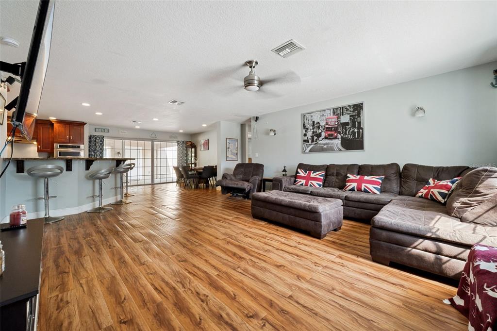 A living room with wood-look flooring, a large sectional sofa, and an open kitchen area — 1050 CRYSTAL BOWL CIRCLE, CASSELBERRY, FL
