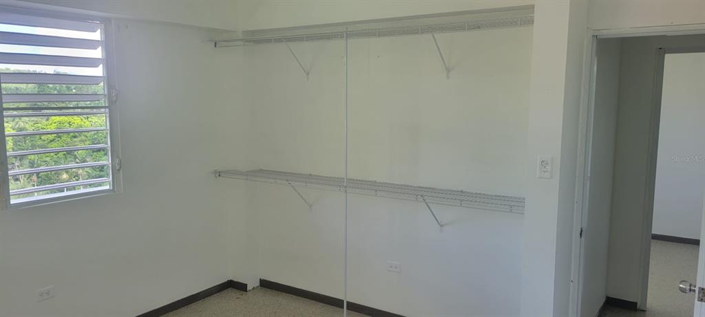 An empty room features white walls, wire shelving, a louvered window, and a doorway — Bo. Ceiba LOS MELENDEZ, CIDRA, PR
