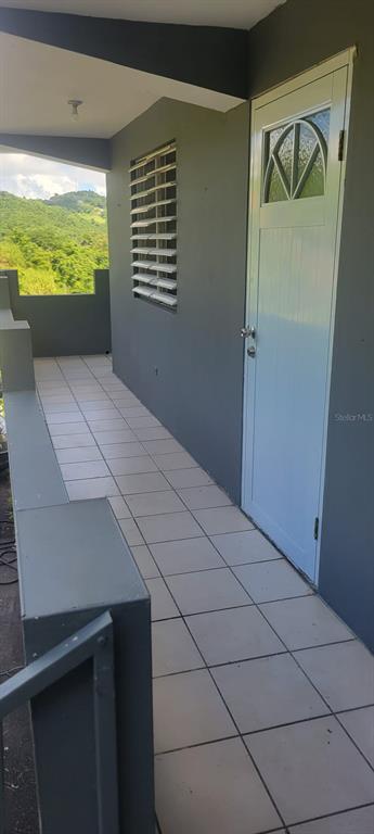 A tiled balcony with a white door and a window with metal shutters overlooks hills — Bo. Ceiba LOS MELENDEZ, CIDRA, PR