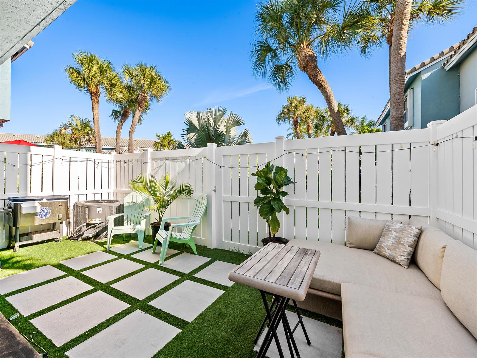 A small patio features a white fence, artificial turf, square pavers, outdoor seating, and palm trees — 1074 Jeffery Street, Boca Raton FL 33487, BOCA RATON, FL