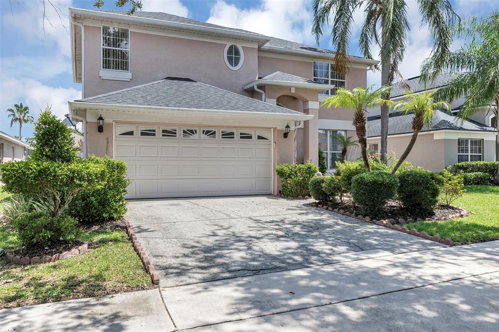 A two-story suburban house with a beige stucco exterior, a two-car garage, and landscaping — 4921 CASA VISTA DRIVE, ORLANDO, FL