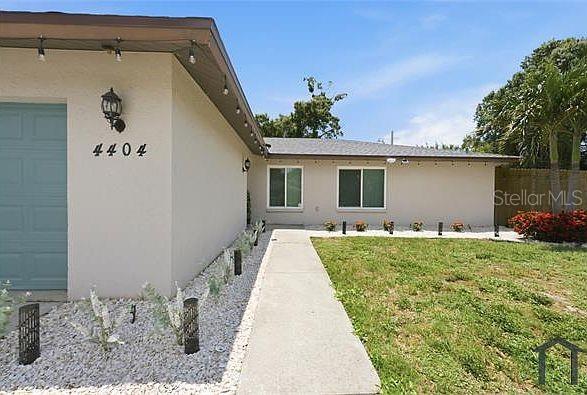 A single-story house exterior features a light-colored facade, a concrete walkway, and gravel landscaping — 4404 MEADOW CREEK CIRCLE, SARASOTA, FL