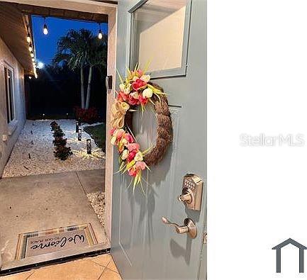A light blue front door with a floral wreath opens to an illuminated outdoor walkway — 4404 MEADOW CREEK CIRCLE, SARASOTA, FL