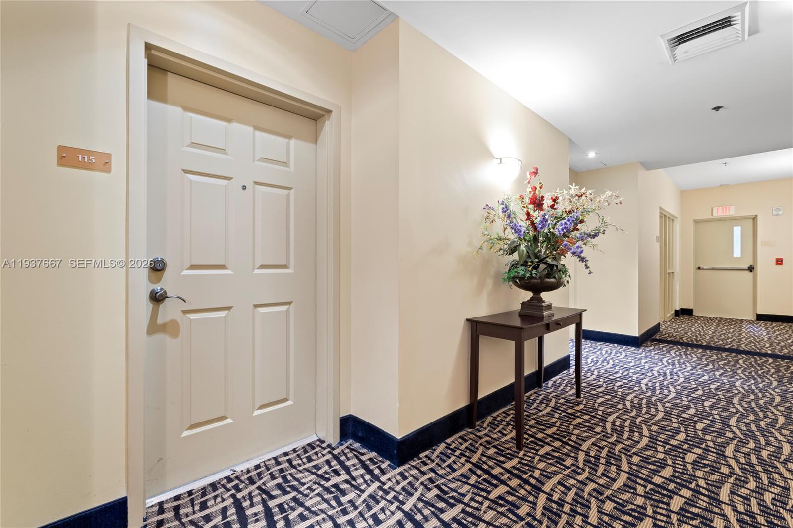 A hallway features a door labeled 115, a decorative floral arrangement on a table, and carpeting — 8395 SW 73rd Ave # 115, Miami FL 33143, MIAMI, FL