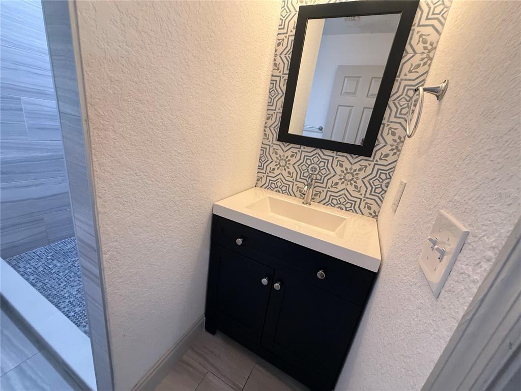 A bathroom features a black vanity, a rectangular sink, and a patterned tile backsplash — 13 VOLUSIA DRIVE, DEBARY, FL