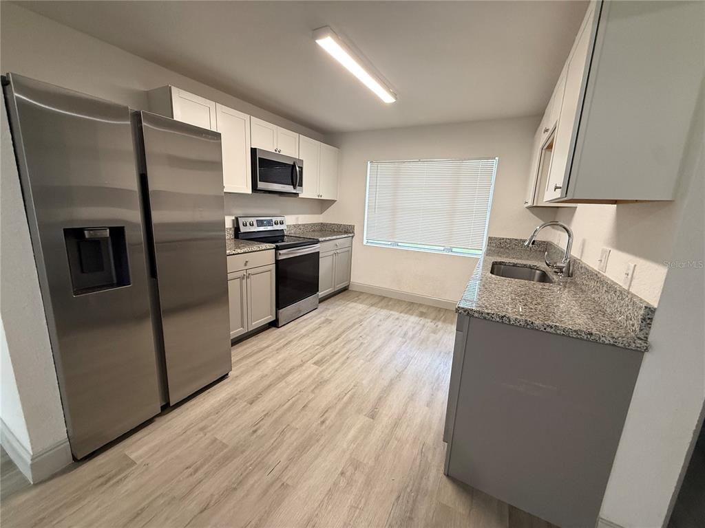 A kitchen features stainless steel appliances, granite countertops, white cabinetry, and light wood-look flooring — 13 VOLUSIA DRIVE, DEBARY, FL