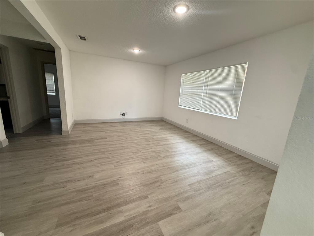 An empty room features light wood-look flooring, white walls, recessed lighting, and a large window — 13 VOLUSIA DRIVE, DEBARY, FL