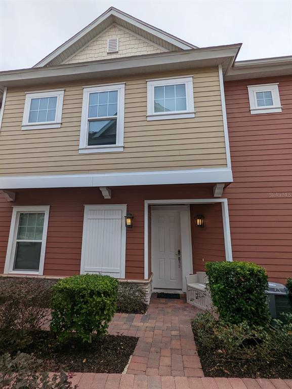 A two-story townhouse exterior features red and tan siding, a white front door, and pavers — 7532 SUNVILLE AVENUE, KISSIMMEE, FL