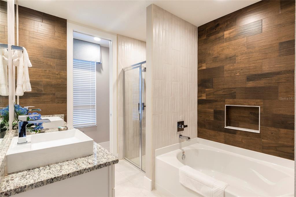 A modern bathroom features a soaking tub, glass-enclosed shower, dual vanity, and wood-look tile walls — 7532 SUNVILLE AVENUE, KISSIMMEE, FL