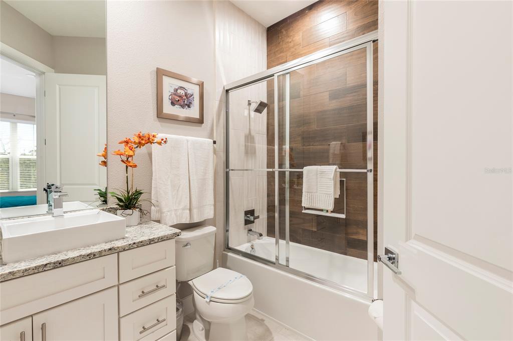A bathroom features a white vanity, a toilet, and a shower-tub combo with wood-look tile — 7532 SUNVILLE AVENUE, KISSIMMEE, FL