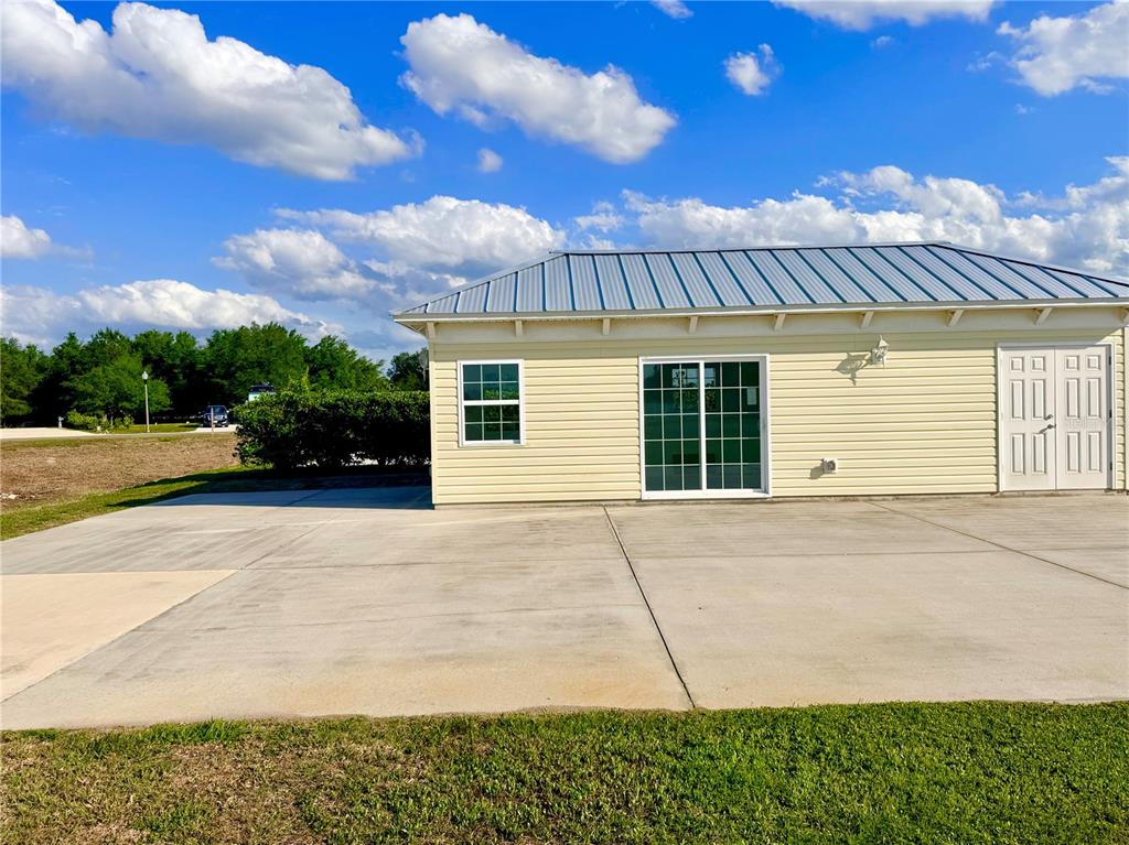 A light yellow building with a metal roof, sliding glass doors, and a concrete driveway — 9381 SE 47TH WAY, WEBSTER, FL