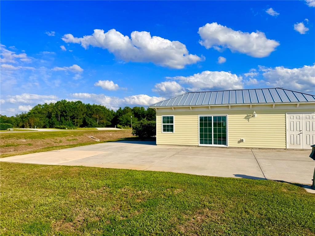A yellow building with a metal roof sits next to a large concrete patio — 9381 SE 47TH WAY, WEBSTER, FL